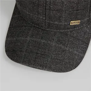 Dettaglio del cappello grigio scuro a quadri con placca metallica dorata del marchio