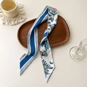 Foulard en soie bleu avec motifs fleurs et papillons sur un plateau en bois