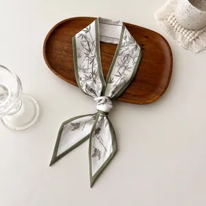 Elegante olijfgroene lange zijden sjaal met bamboe- en vlinderprints op een houten dienblad