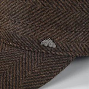 Brown herringbone winter flat cap with thick wool texture and a peak metal badge