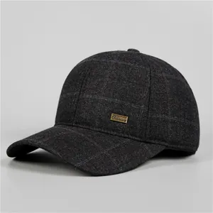 Dettaglio del tessuto a quadri grigio scuro e logo in metallo dorato sul cappello invernale