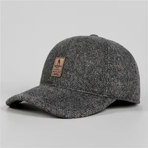 Detailed view of dark grey herringbone tweed winter baseball cap with leather logo patch
