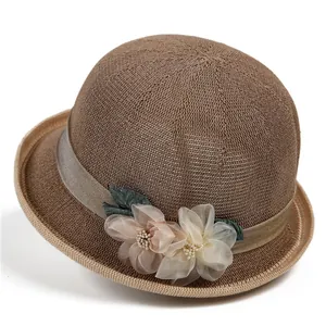 Eleganter Damen-Strickhut in Kaffee-Farbe mit Satinblumen-Deko vor weißem Hintergrund