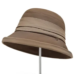 Detail of a brown pleated sun hat showing premium fabric texture and small metal logo buckle