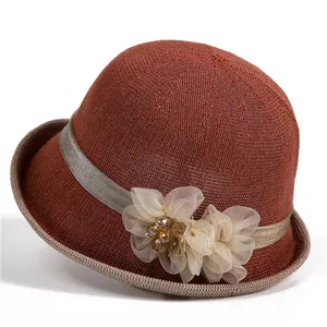Detail eines burgunderroten Strickhutes mit eleganter Schleife und floralen Perlenverzierungen