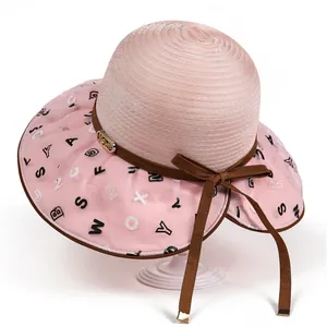 Detail of pink sun hat featuring letter print brim, brown ribbon bow and gold LOVE buckle