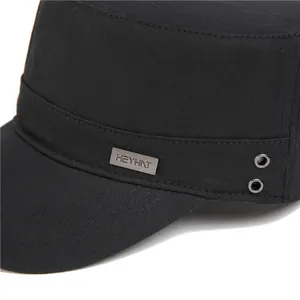 Detail of a black cotton cadet cap with a metal logo plate and breathable air eyelets