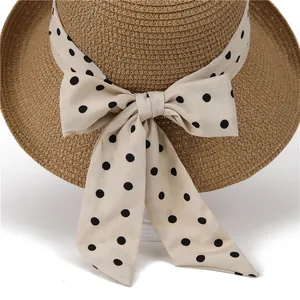 Close-up of beige woven straw hat featuring a cream ribbon with black polka dots and bow