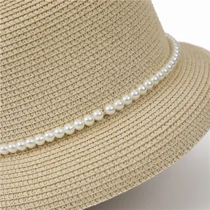 Close-up of woven straw sun hat featuring elegant white pearl bead band detail