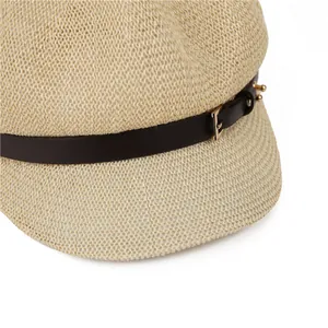 Close-up of beige woven paper newsboy hat with brown leather strap and gold buckle detail