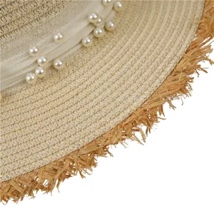 Detail of woven straw hat featuring elegant faux pearls and frayed edge texture