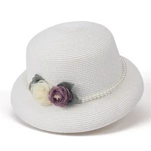 Detail of hand-crafted fabric flowers and pearl chain on a white straw sun hat