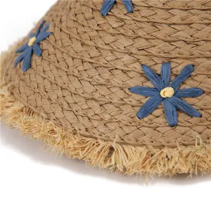 Detail of straw sun hat with handmade blue floral decor and fringe brim textures