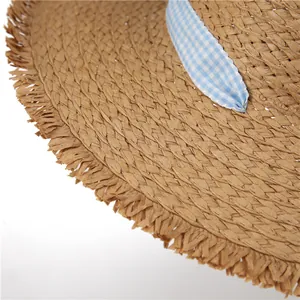 Close-up of woven straw sun hat with frayed edges and blue gingham ribbon detail