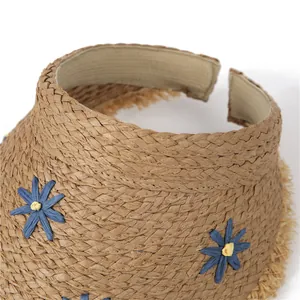 Close-up of woven straw sun hat with blue daisy appliques and frayed brim texture