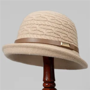 Detail of knit cloche hat with beige cable texture, brown leather strap and gold buckle