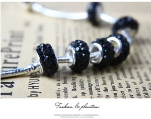 Detail of black crystal charms on silver snake chain bracelet over vintage newspaper