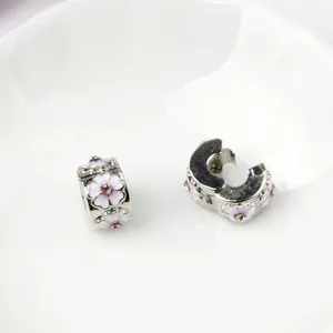 Pink and white enamel magnolia flower charms on a white ceramic plate for DIY bracelets