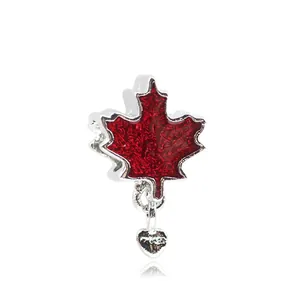 Macro detail of red maple leaf charm in silver with a small dangling heart pendant