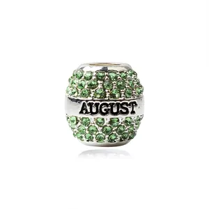 Détail macro d'une perle charm argentée avec cristaux verts et gravure August