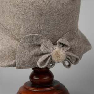 Elegant oatmeal wool cloche hat for elderly women with fur pom-pom bow on a wooden stand