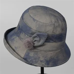 Close-up of blue-grey tie-dye bucket hat with fabric bow and grey pom-pom detail