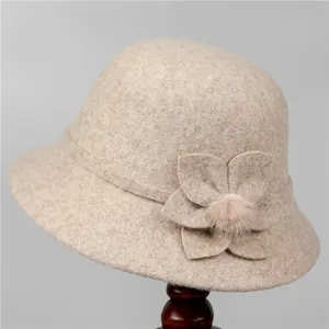 Detail of beige wool felt cloche hat featuring a floral ornament and pink fuzzy pom-pom