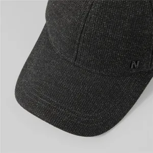 Close-up of winter wool cap texture with black metal N logo on dark charcoal fabric