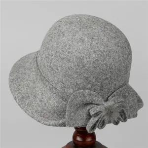 Detail view of a grey wool cloche hat with a bow and fur ball on a wooden stand