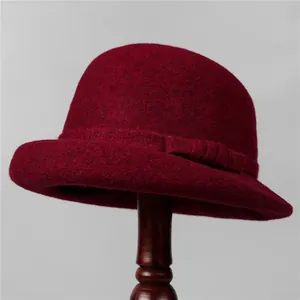 Close-up of deep red wool felt cloche hat with rolled edge and bow detail on wooden stand