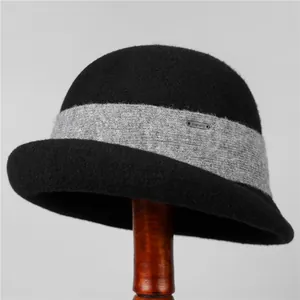 Detailed texture of black wool cloche hat with grey knitted band and metal logo on stand