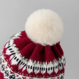 Détail du bonnet en tricot bordeaux avec jacquard géométrique et pompon en fausse fourrure