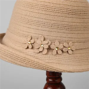 Elegante cappello cloche in maglia beige con fiori decorativi su supporto legno