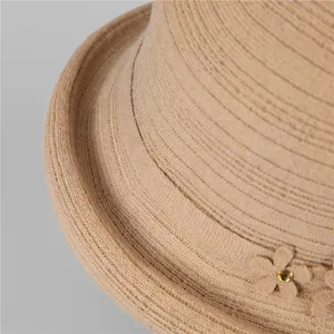 Dettaglio ravvicinato del cappello a secchiello beige con trama intrecciata e fiore decorato