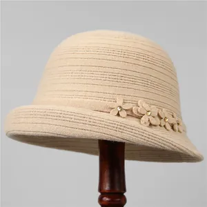 Dettaglio di un cappello cloche in maglia beige con fiori decorativi e perle dorate