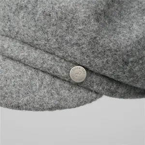 Close-up of grey wool newsboy cap featuring an engraved metallic button detail