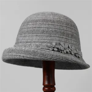 Dettaglio di un cappello a secchiello in maglia grigia con fiori decorativi e perle