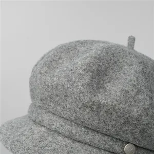 Detailed shot of grey wool newsboy hat featuring a silver metal button and tweed texture