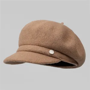 Detailed close-up of brown wool newsboy hat featuring textured fabric and a silver metal badge