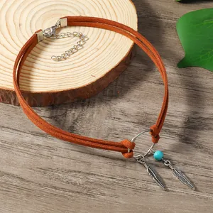 Détail du collier bohème avec cordons en daim marron, plumes argentées et perle turquoise