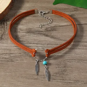 Gros plan d'un choker ethnique avec plumes en métal et perle turquoise sur bois