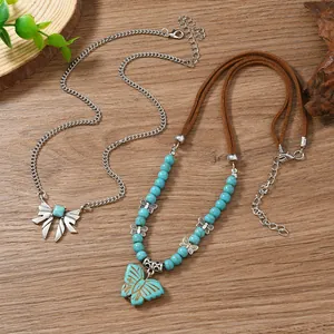Détail de 2 colliers pendentifs papillon avec perles turquoise sur fond en bois naturel