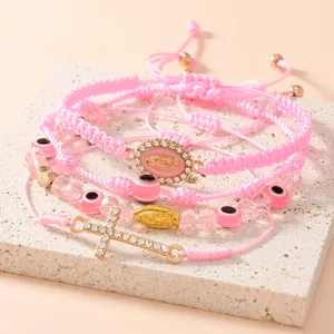 Dettaglio di braccialetti religiosi intrecciati rosa con croce, malocchio e medaglie
