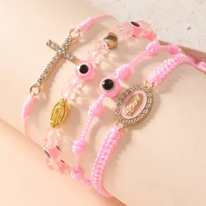 Vista macro dei braccialetti rosa intrecciati con medaglia della Madonna e ciondolo a croce