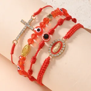 Dettaglio di bracciali rossi intrecciati con croce, occhio greco e medaglia di Maria