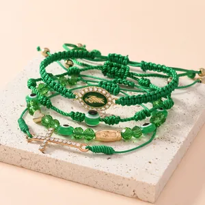 Dettaglio di braccialetti intrecciati verde smeraldo con malocchio e croce dorata