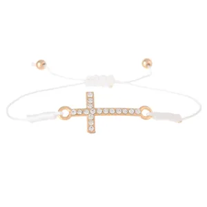 Dettaglio del bracciale intrecciato bianco con croce dorata e pietre di zirconia cubica
