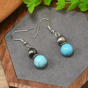 Detailed shot of Bohemian turquoise drop earrings with bull skull charm in wood tray