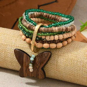 Detalle de pulsera bohemia con cristales verdes y un colgante de mariposa de madera tallada