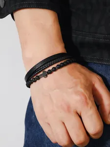 Detalle de conjunto de tres pulseras para hombre de cuero negro con perlas y cruz